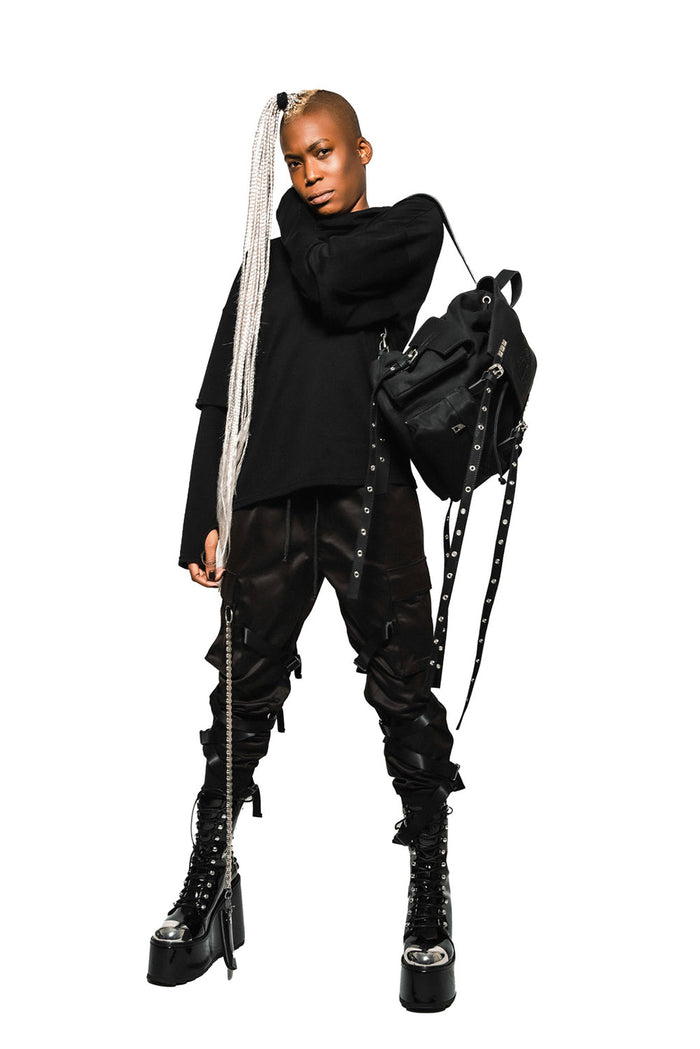 Person wearing a black outfit with high boots and a punk backpack on a white background
