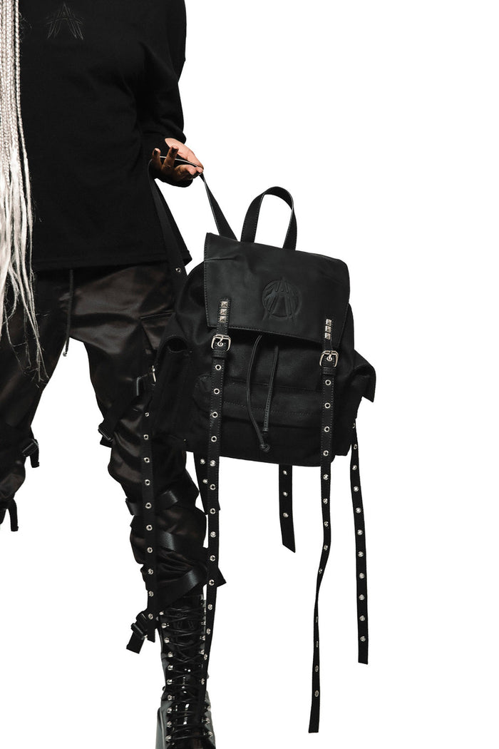 Black backpack with straps held by a person wearing black clothing on a white background