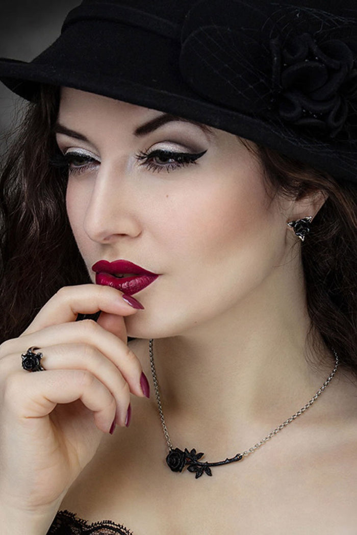 Woman wearing a black hat with floral details and a necklace, posing thoughtfully.