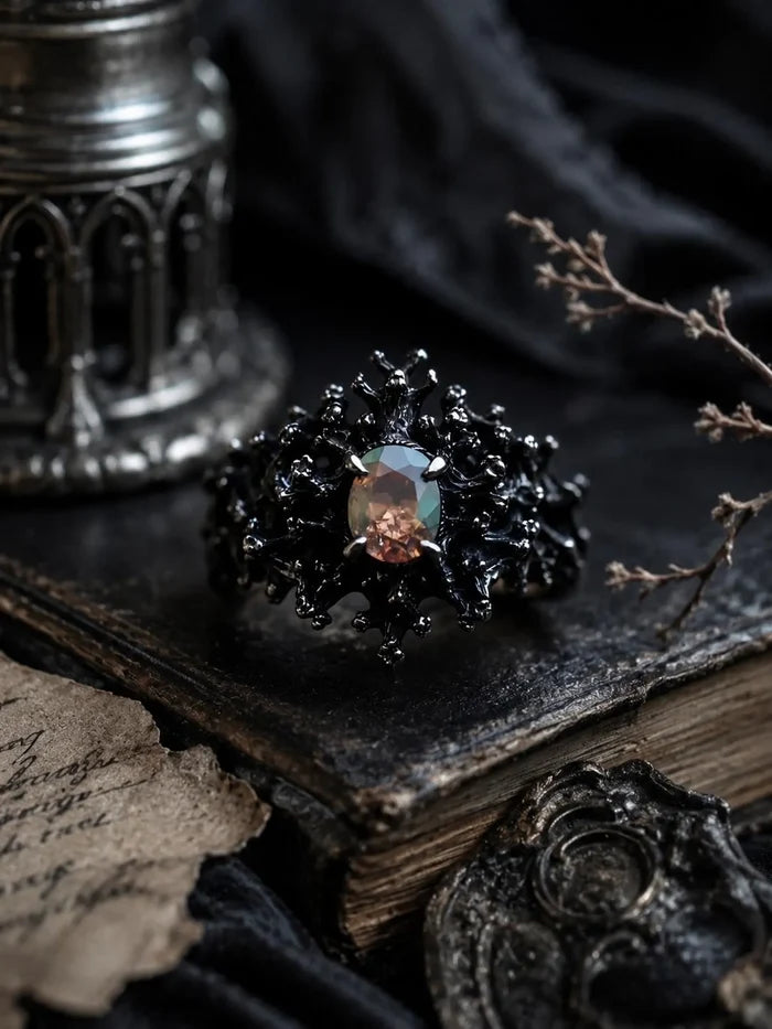 Dark Bloom Ring — black oxidized 925 sterling silver bloom of thorns and coral around an iridescent oval opal, on a dark book