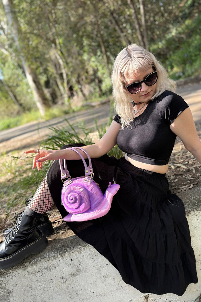 Person holding a purple snail-shaped handbag outdoors