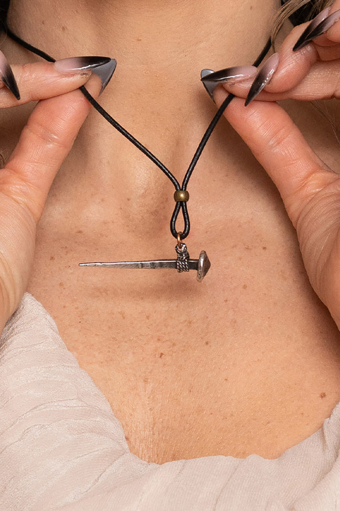 Necklace with a nail pendant being held against skin