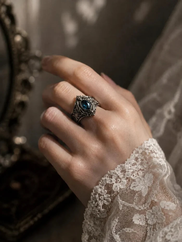 Hand wearing Victorian memento mori skull ring with blue topaz — gothic alternative engagement ring in 925 silver